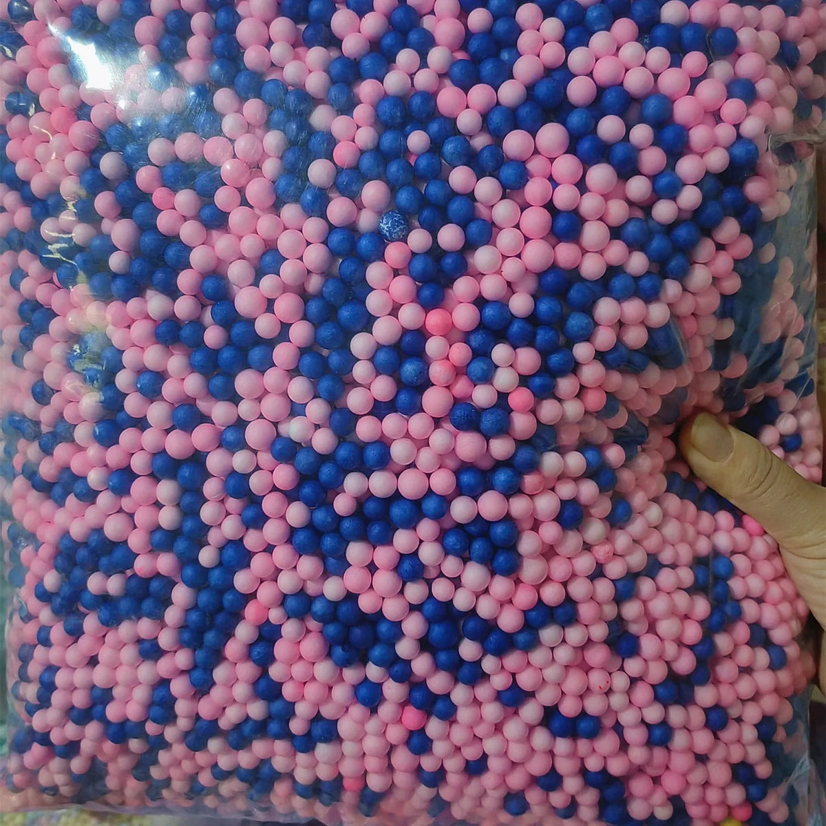 A close-up view of a large quantity of pastel pink and blue foam beads for crafting and decoration.