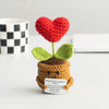 Handmade crochet plant decoration featuring a red heart flower and green leaves on a brown body.