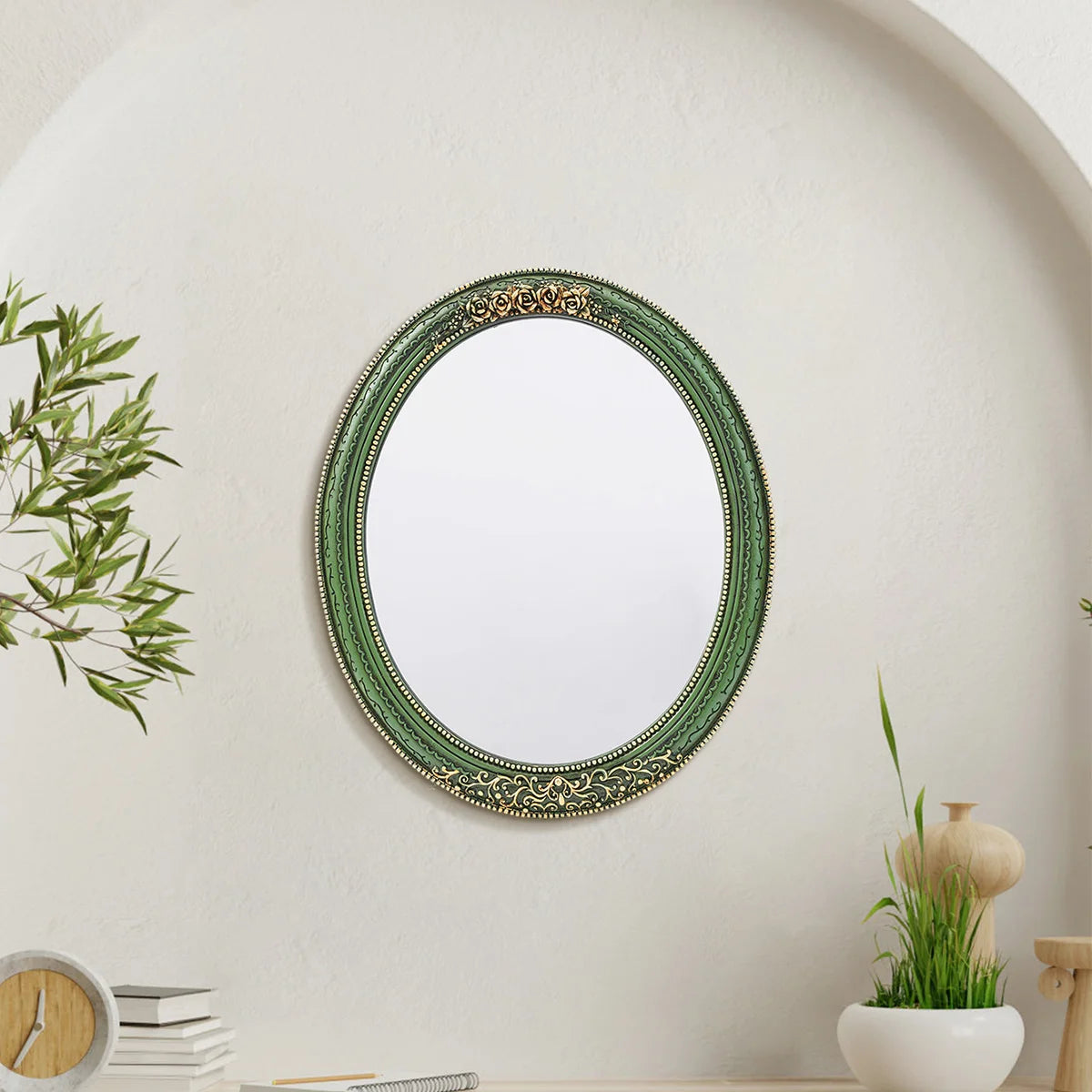An oval wall mirror with a green frame featuring intricate lace design mounted on a white wall.