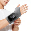 A person is holding a gray wrist massager with a digital display and vibration features.