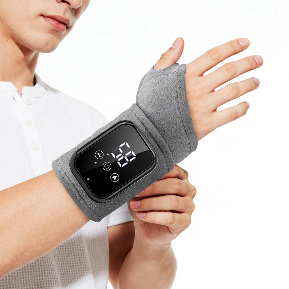 A person is holding a gray wrist massager with a digital display and vibration features.