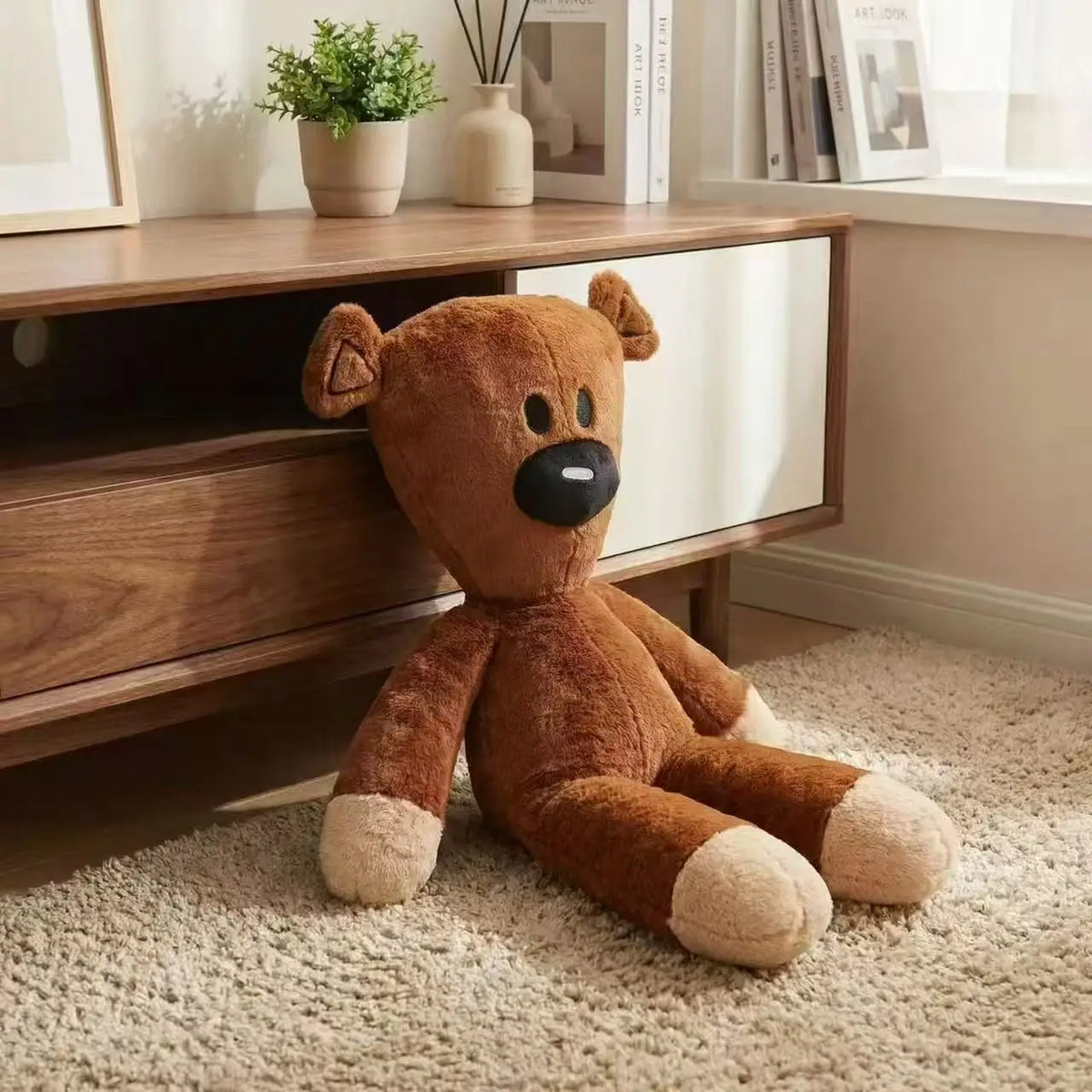 A brown teddy bear stuffed plush toy sitting on a light beige carpet next to wooden shelving.