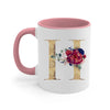 A pink ceramic coffee mug featuring a gold letter initial decorated with a floral arrangement.