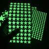 A hand holds up a sheet of glow-in-the-dark wall stickers featuring green stars against a dark background.