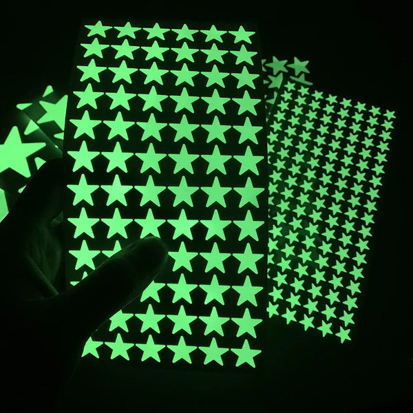 A hand holds up a sheet of glow-in-the-dark wall stickers featuring green stars against a dark background.