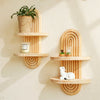 A set of geometric wooden wall shelves displaying a potted plant, a candle, and a small figurine.