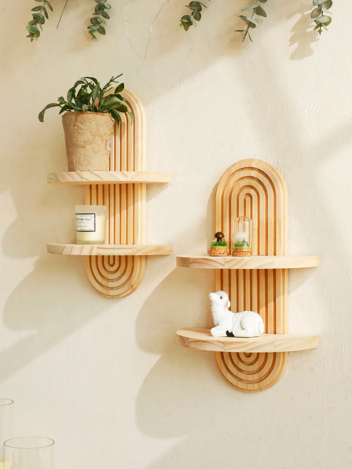 A set of geometric wooden wall shelves displaying a potted plant, a candle, and a small figurine.