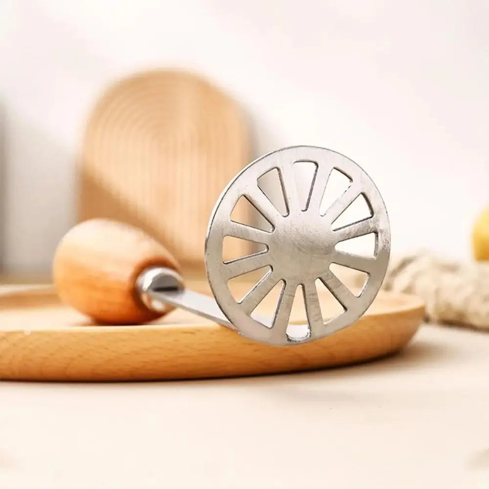 Silver slotted potato and pumpkin masher with a wooden handle resting on a light wooden board.