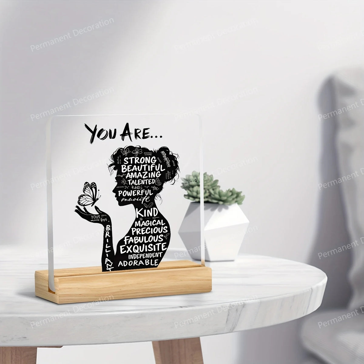 A clear acrylic sign with black text reading You Are Strong Beautiful Amazing Talented Powerful Unique Kind Magical Precious 