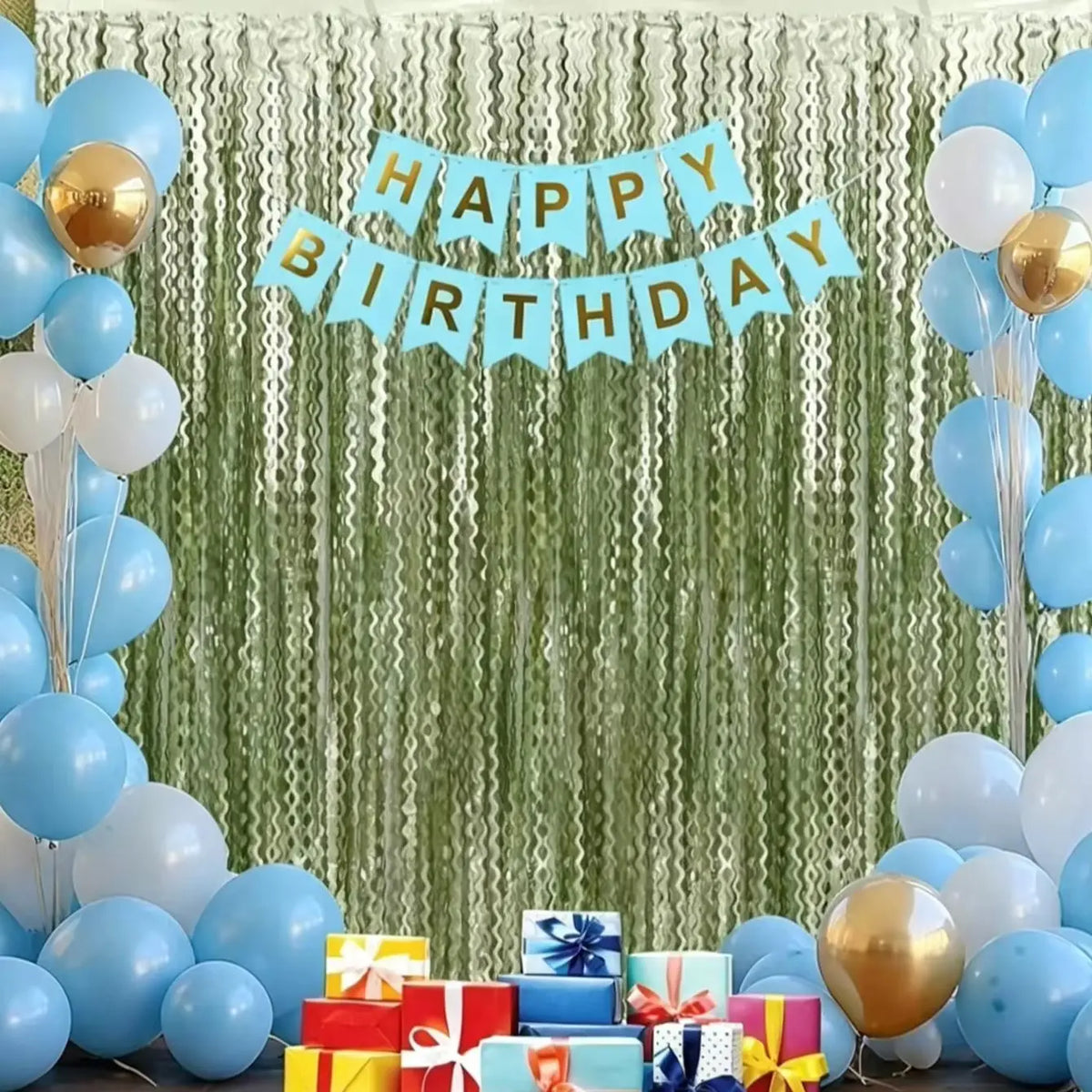 A birthday banner made of light blue paper flags hangs in front of a green wavy curtain backdrop decorated with balloons and 