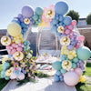 A large balloon arch display featuring pastel macaron balloons in shades of purple, blue, pink, and yellow.