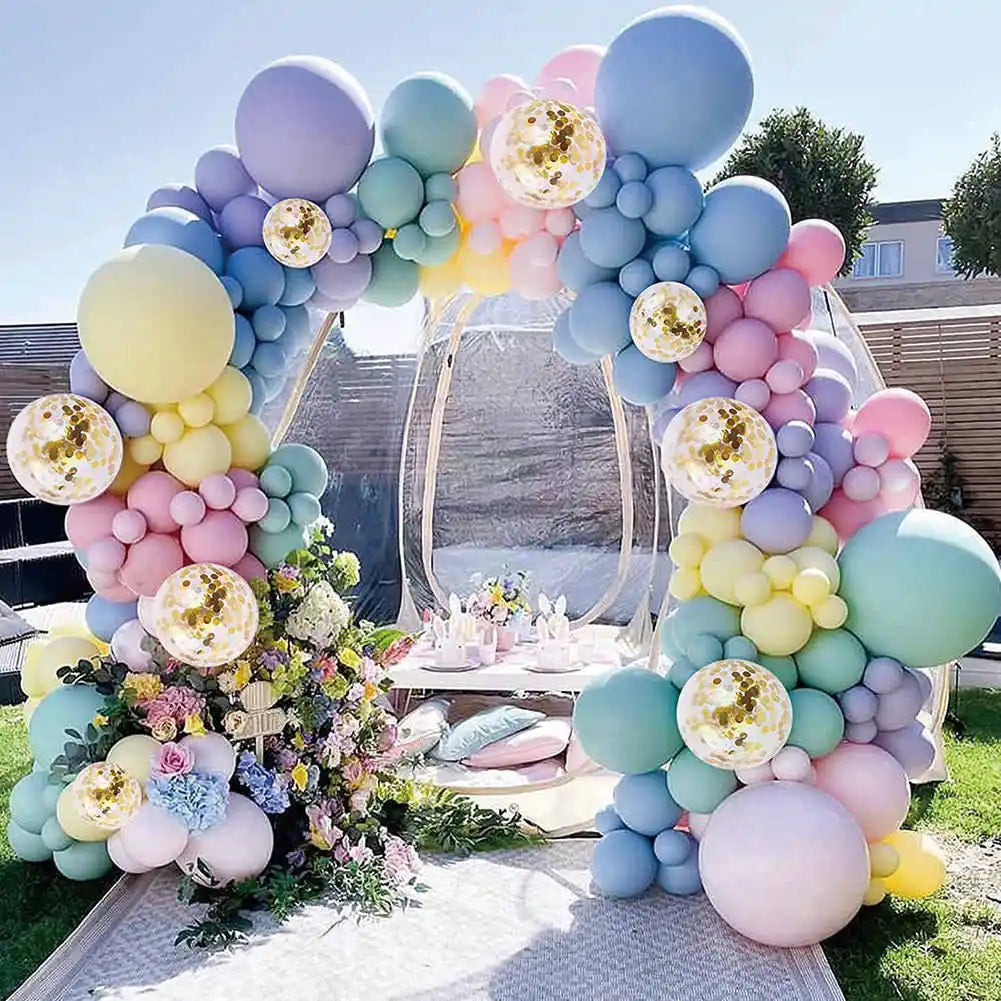A large balloon arch display featuring pastel macaron balloons in shades of purple, blue, pink, and yellow.