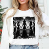 A white sweatshirt featuring a black and white illustration of several witches standing in a forest silhouette.