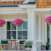 A porch decorated with hanging pink silk flowers in terracotta pots and a wreath on a wooden door.