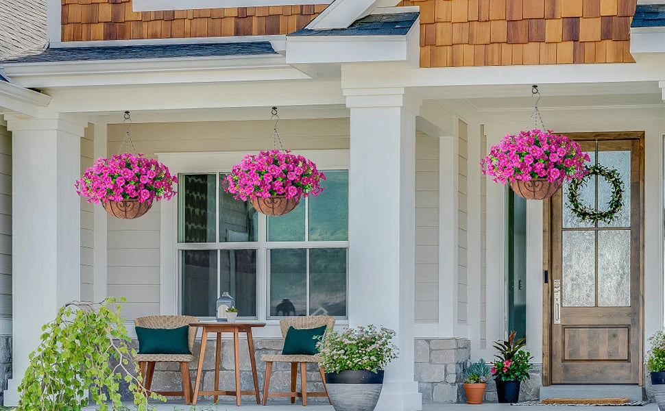 A porch decorated with hanging pink silk flowers in terracotta pots and a wreath on a wooden door.