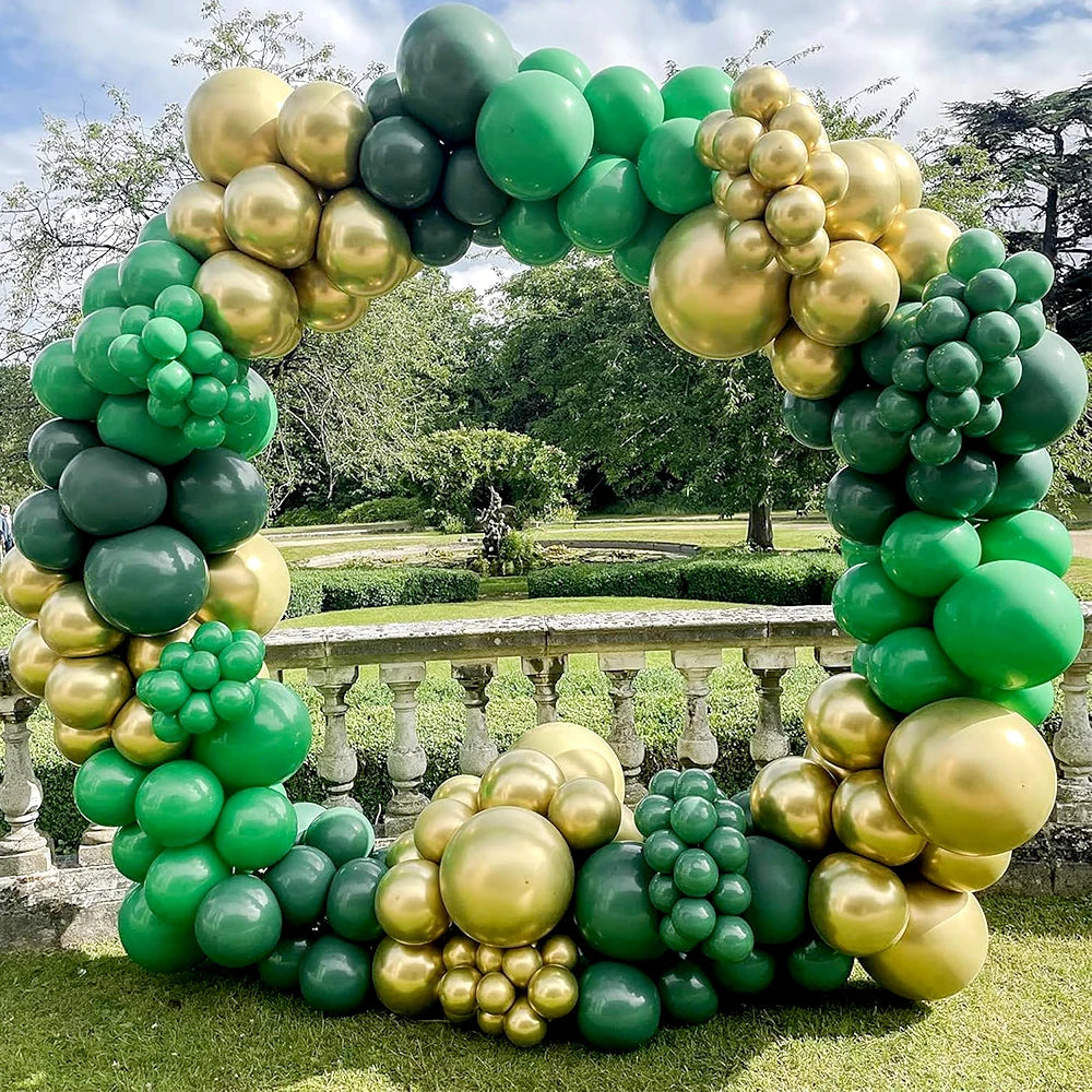 An archway made of green and gold latex balloons for party decor set in a grassy outdoor setting.