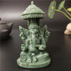A small, green bronze statue of Ganesha Buddha with a tiered umbrella top sitting on a dark surface.