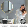 A woman is looking in a large round vanity mirror with a matte metal frame, demonstrating the product's features.