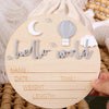 A wooden birth announcement sign featuring a crescent moon, a hot air balloon, and the text hello world.
