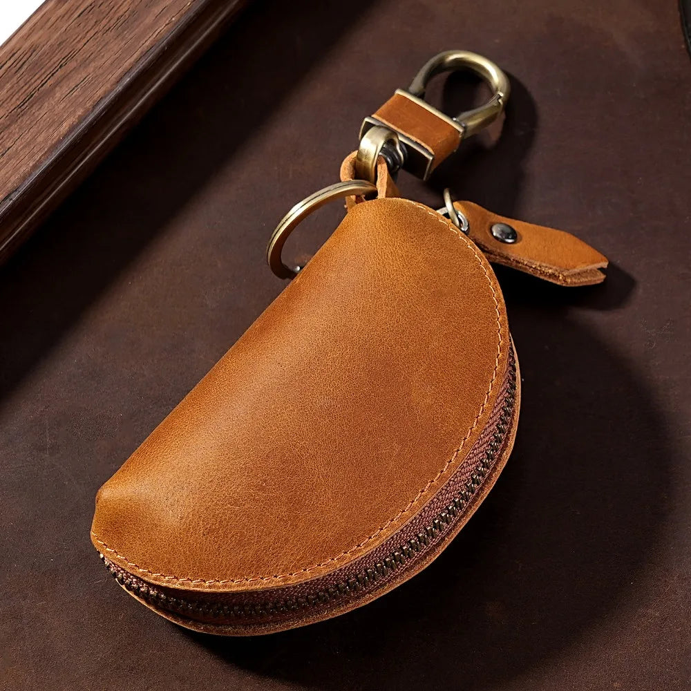 A brown leather key pouch with a brass carabiner attached, resting on a dark surface.