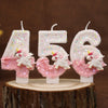 Velas de purpurina rosa y blanca con forma de los números 456, exhibidas sobre una superficie de madera.
