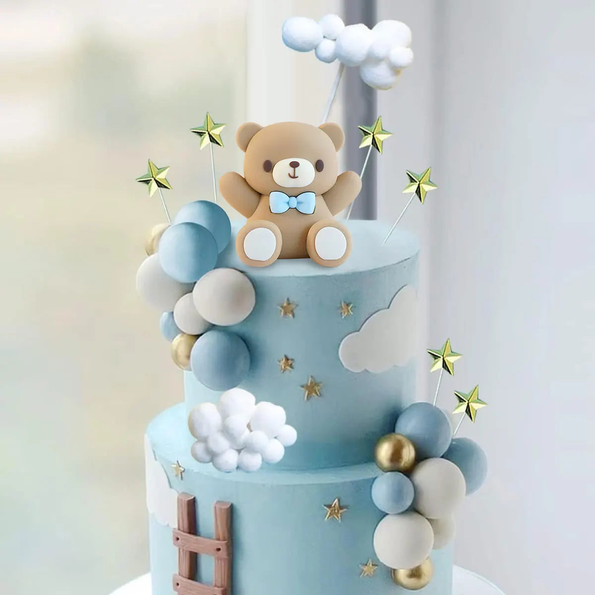 A two-tiered light blue cake decorated with clouds, stars, and a teddy bear topper.