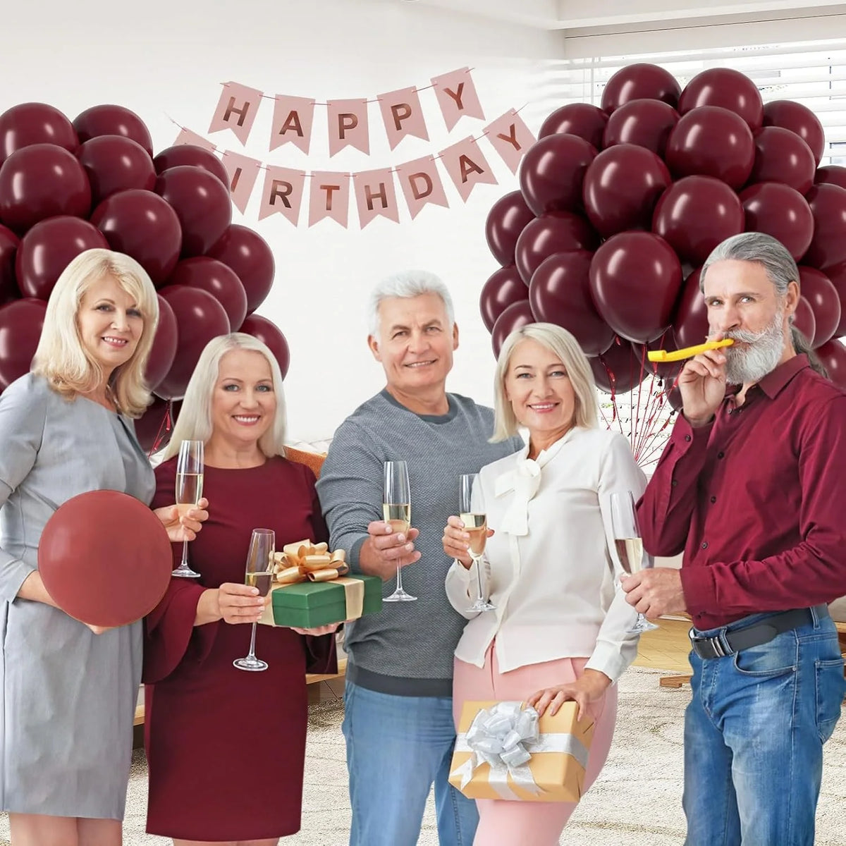 A family of four celebrating a birthday with a large arrangement of burgundy red latex balloons.