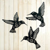 A set of three black metal hummingbird wall decor silhouettes against a light wooden background.