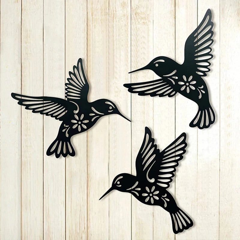 A set of three black metal hummingbird wall decor silhouettes against a light wooden background.