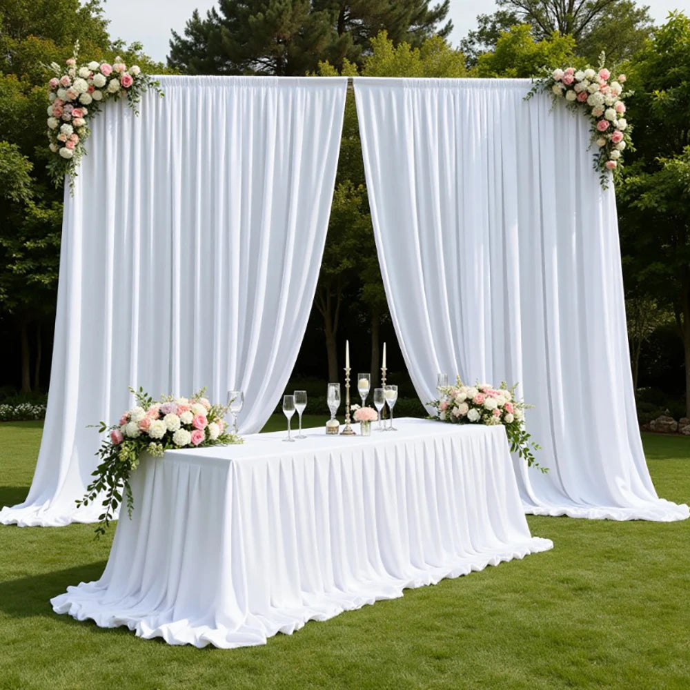 A white fabric backdrop curtain decorated with floral arrangements set up outdoors for an event.
