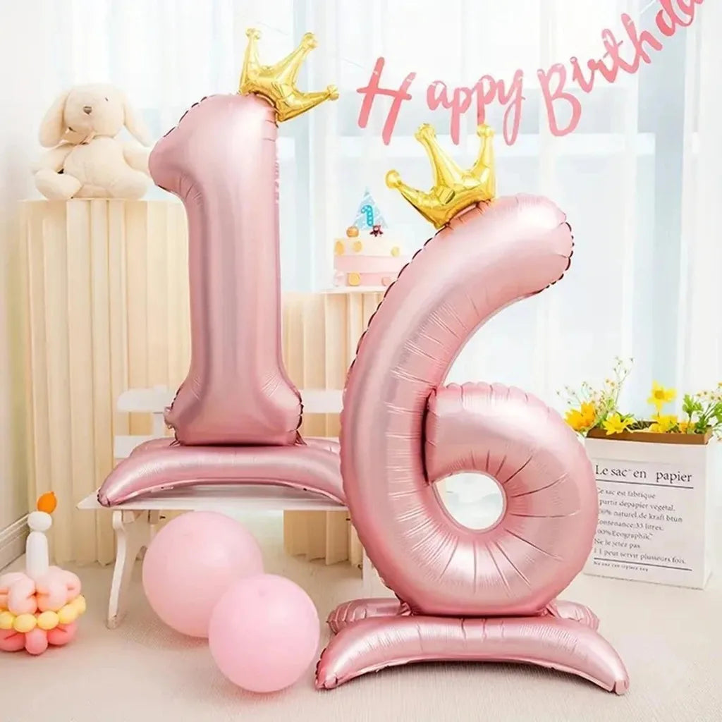 Pink foil number balloons spelling '16' with gold crowns and pink confetti