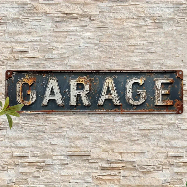 A weathered, dark metal sign with the word GARAGE mounted on a light-colored stone wall.
