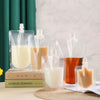 A collection of clear reusable squeezable liquid drink pouches filled with various colored juices and milk.
