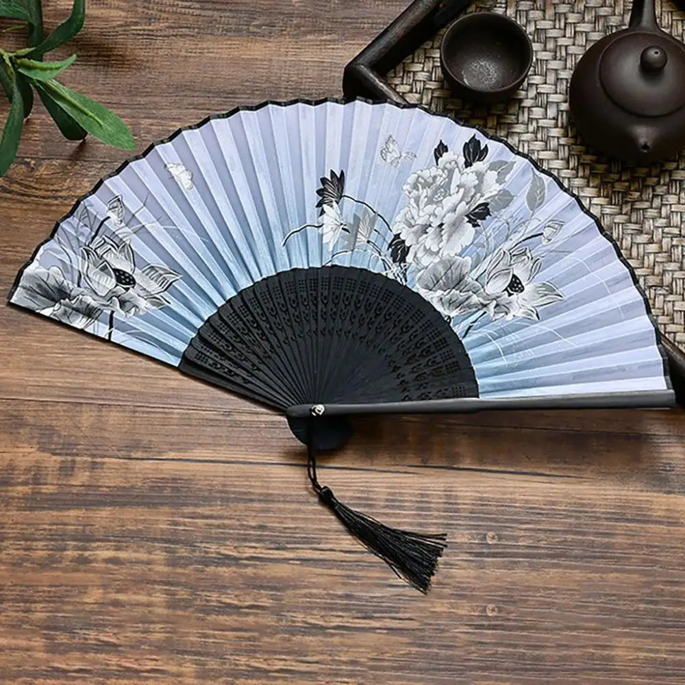 A vintage silk folding fan with blue and white floral patterns rests on a wooden surface.