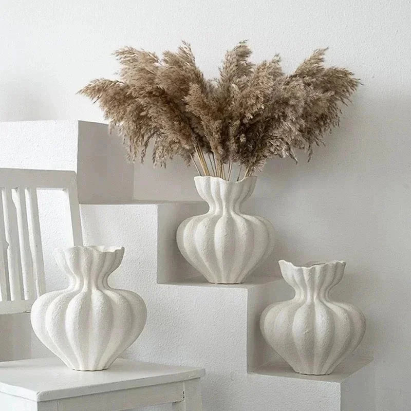 A display of white ceramic vases and dried ornamental grasses on a white shelf.