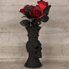 A bouquet of deep red roses in black foliage displayed in a skull-shaped decorative vase.
