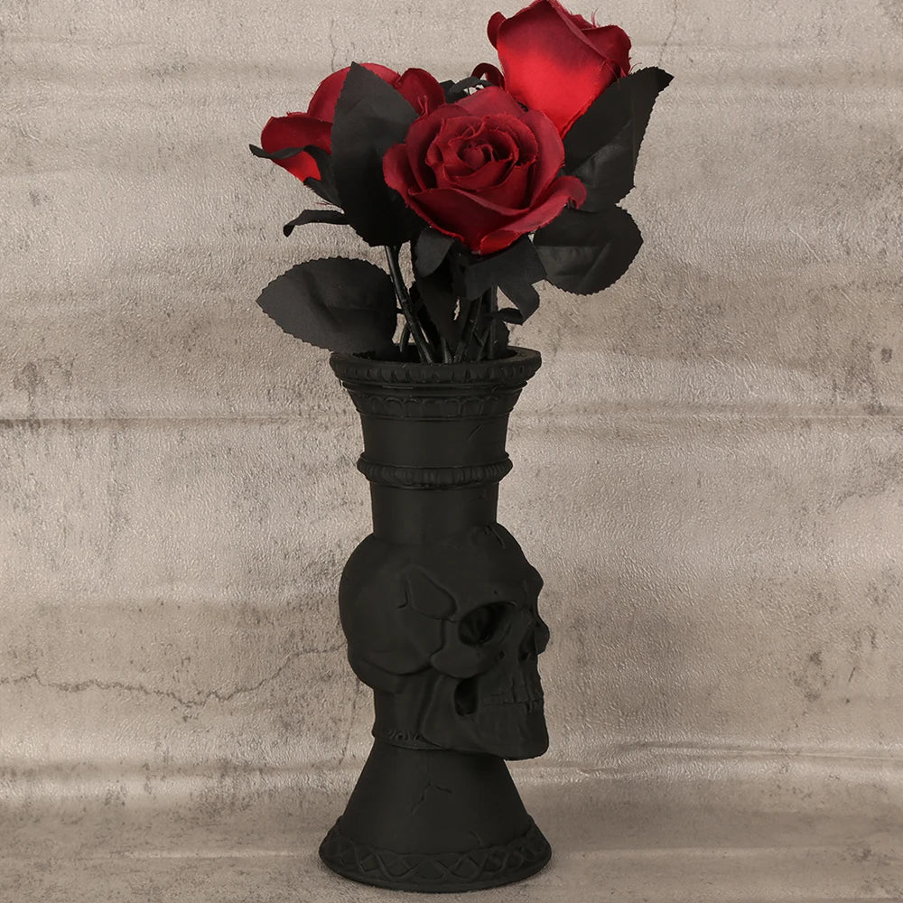 A bouquet of deep red roses in black foliage displayed in a skull-shaped decorative vase.