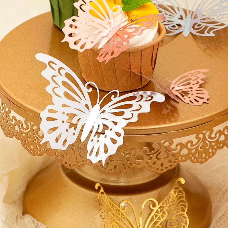 A tiered gold stand displays decorative 3D butterfly wall stickers in white, pink, and yellow on a cupcake.