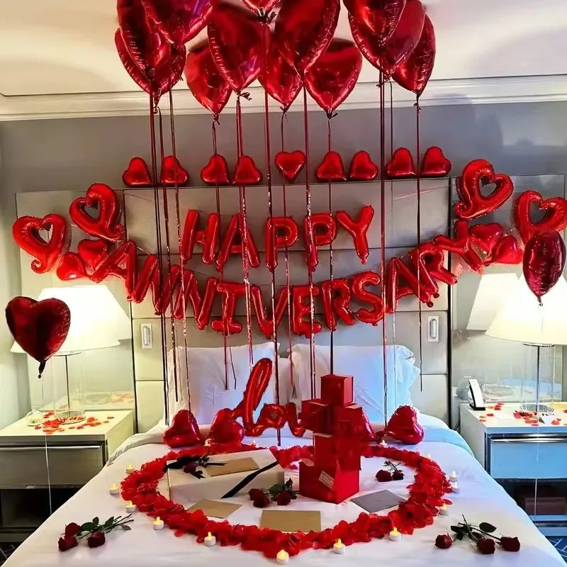 A bed decorated with red foil balloons and a large banner spelling out Happy Anniversary