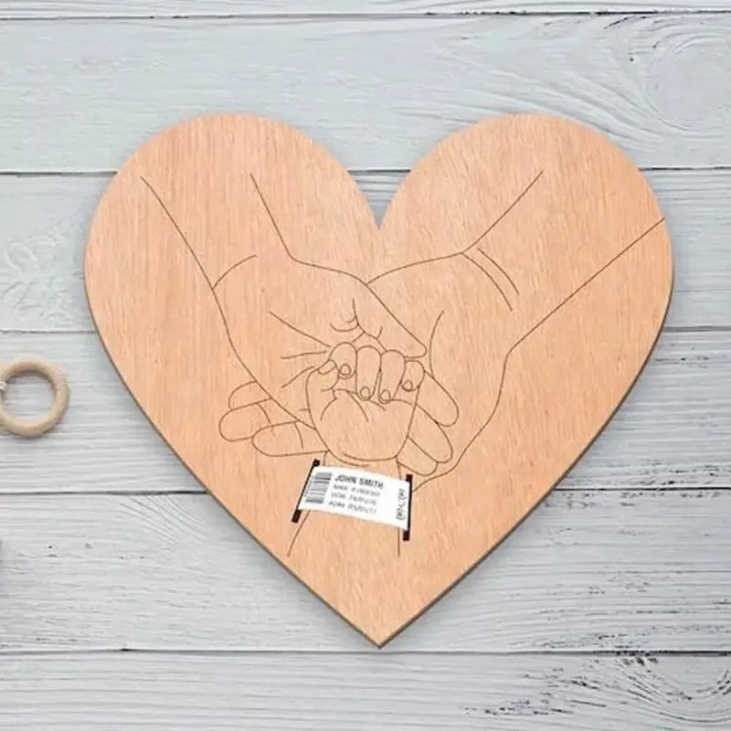 A wooden heart-shaped sign featuring a line drawing of two hands, intended as a personalized newborn hospital keepsake.