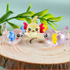 A collection of mini resin axolotl figurines in various pastel colors resting on a wooden slice with green leaves in the back