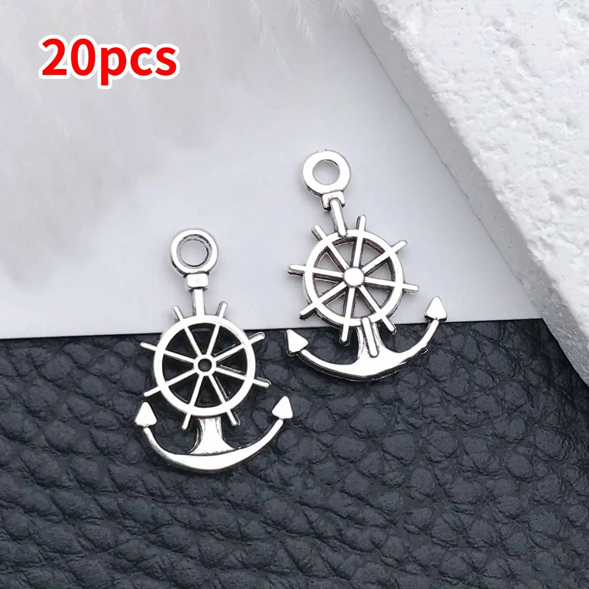 A pair of silver vintage ship anchor charms for jewelry making displayed on a dark surface.