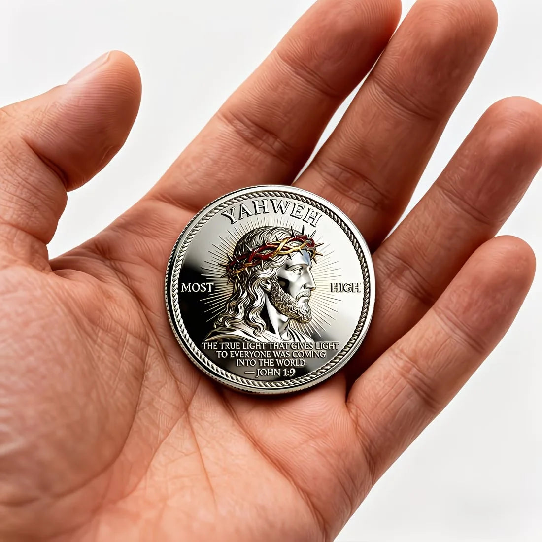 A hand holds a silver faith challenge coin featuring the name Yahweh and a crown of thorns design.