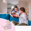 A woman is placing a heartfelt acrylic heart plaque on another woman's chest in a bright living room setting.