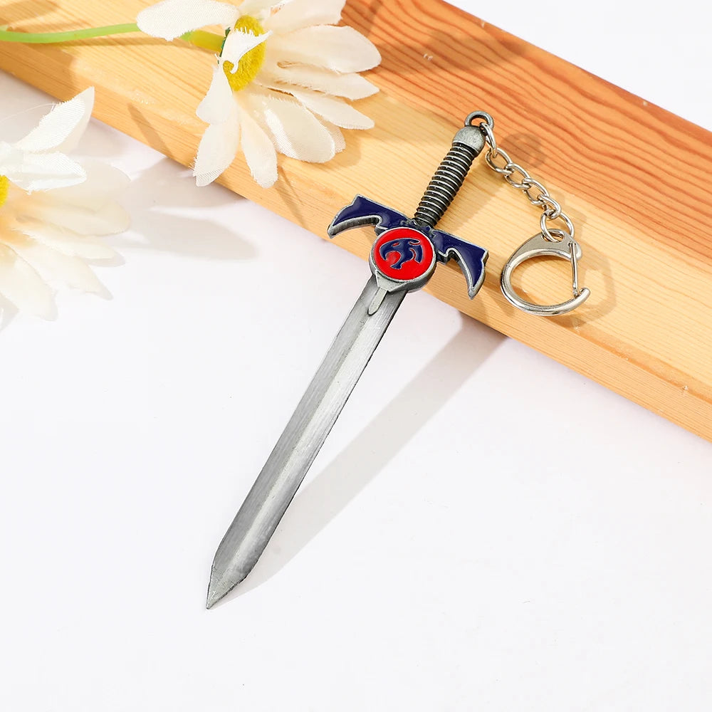 A silver Thundercats metal lion mark sword keychain with a red and blue pendant resting on a wooden surface.