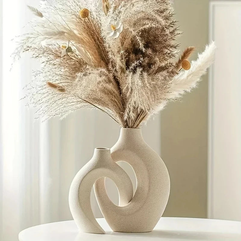 A dried floral arrangement in a beige vase on a white surface.