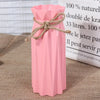 Pink plastic vase with a natural twine bow tied around the neck, displayed next to a white informational sign.
