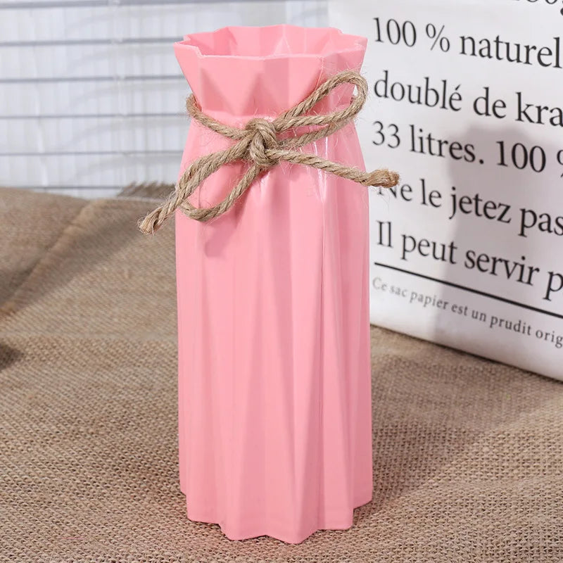 Pink plastic vase with a natural twine bow tied around the neck, displayed next to a white informational sign.