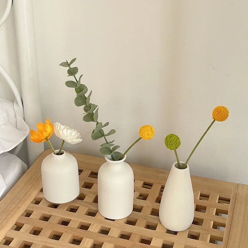 Three white ceramic mini flower vases holding green leafy stems on a wooden tray.