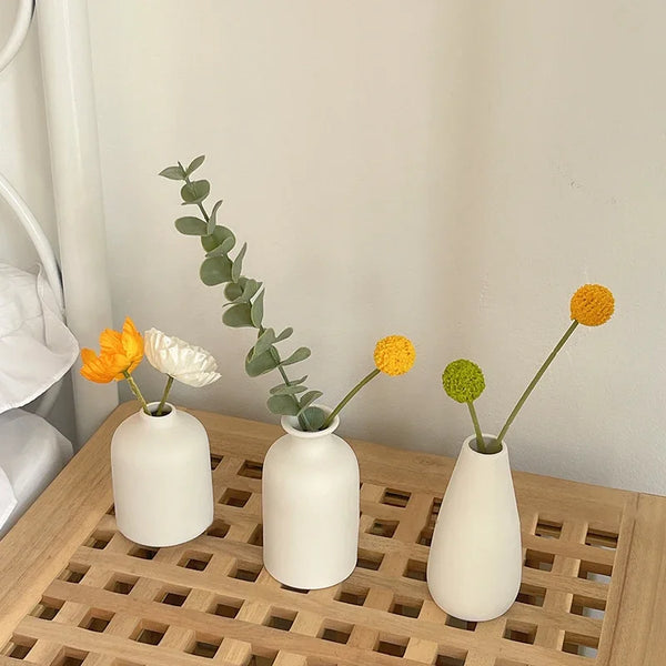 Three white ceramic mini flower vases holding green leafy stems on a wooden tray.